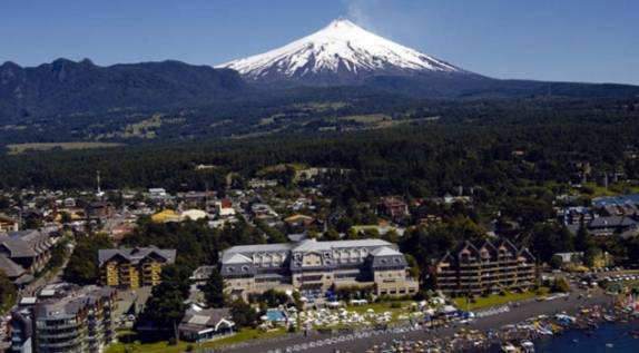 Foto aérea de Pucón onde se destaca, além do vulcão Villarrica ao fundo, o mais tradicional hotel da cidade, o Gran Hotel, em frente à praia de areias escuras do lago Villarrica (foto da internet)